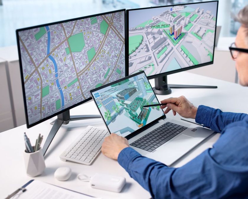 Cartographer analyzing city maps on dual monitors and tablet at a white desk