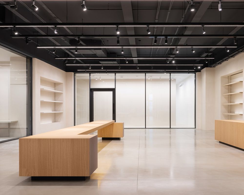 Modern minimalist showroom with light wood tables, white shelves, and black ceiling beams
