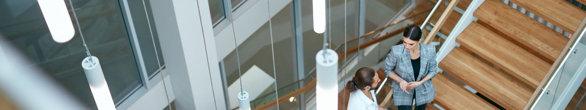 People walking up and down a modern indoor staircase with glass railings and wooden steps.