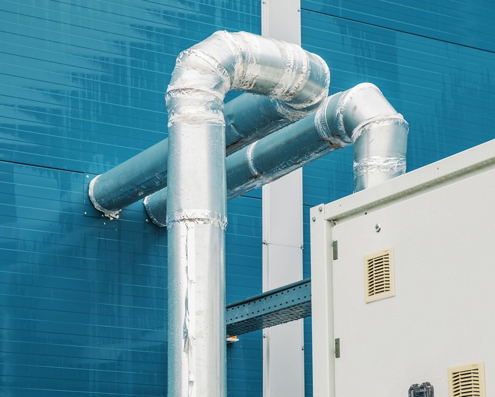 Insulated silver pipes against a blue wall beside a white utility cabinet
