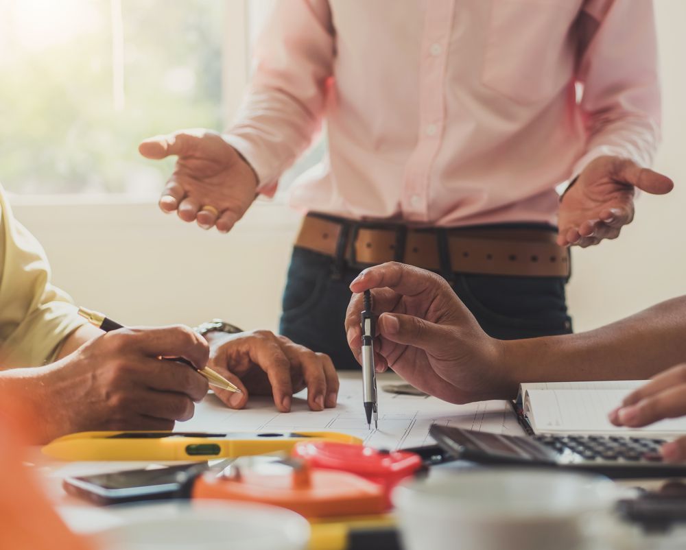 Colleagues in a meeting pointing at documents and calculator on a desk