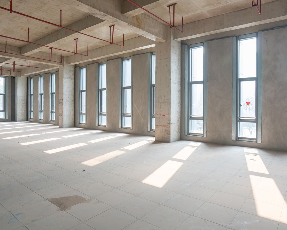 Empty modern room with large windows, concrete columns, and sunlight streaming across the floor