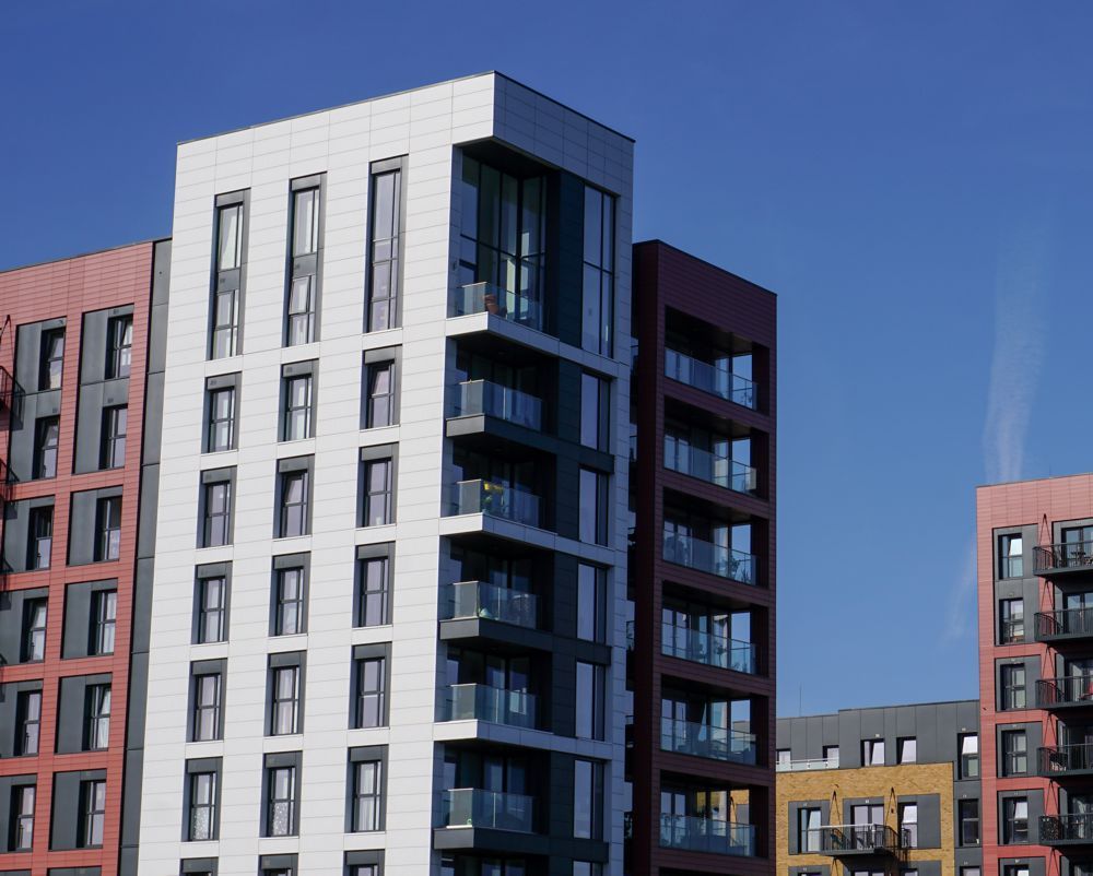 Modern apartment buildings with white, red, and dark facades against a clear blue sky