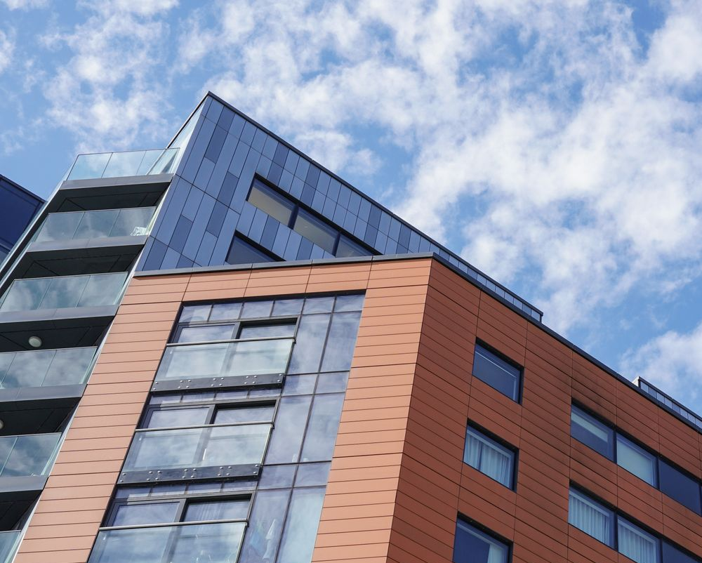 Modern glass and brick building viewed from below against a blue sky with clouds
