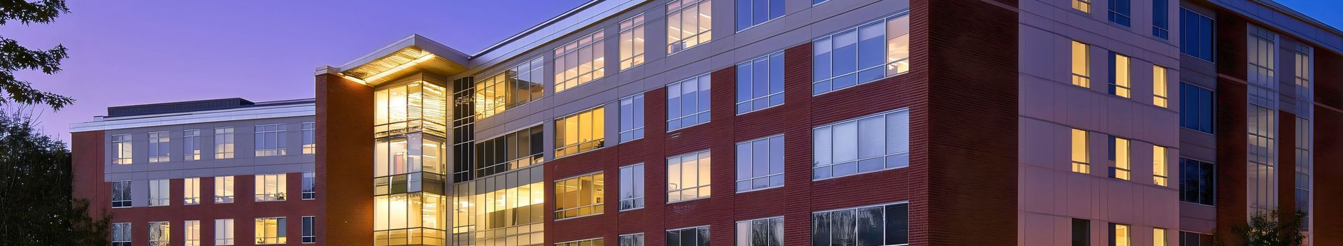 Modern brick apartment building at dusk with lit windows and a glass entryway