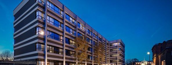 Modern apartment buildings at dusk under a blue sky, lit windows and streetlights visible