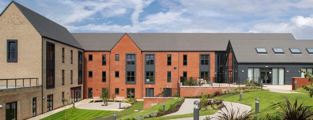 Modern apartment complex with red brick buildings, landscaped courtyard, and blue sky