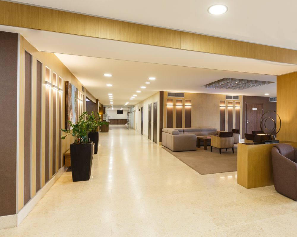 Modern hotel lobby with beige walls, recessed lighting, potted plants, and seating areas
