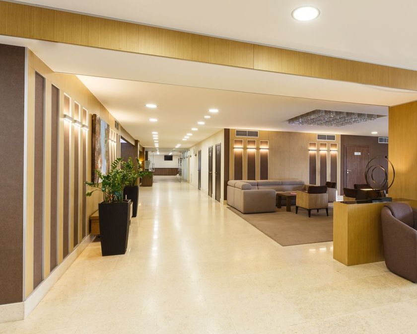 Modern hotel lobby with beige floors, wood accents, potted plants, and seating area under recessed lighting