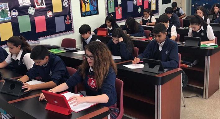 A group of students are sitting at desks in a classroom using laptops.