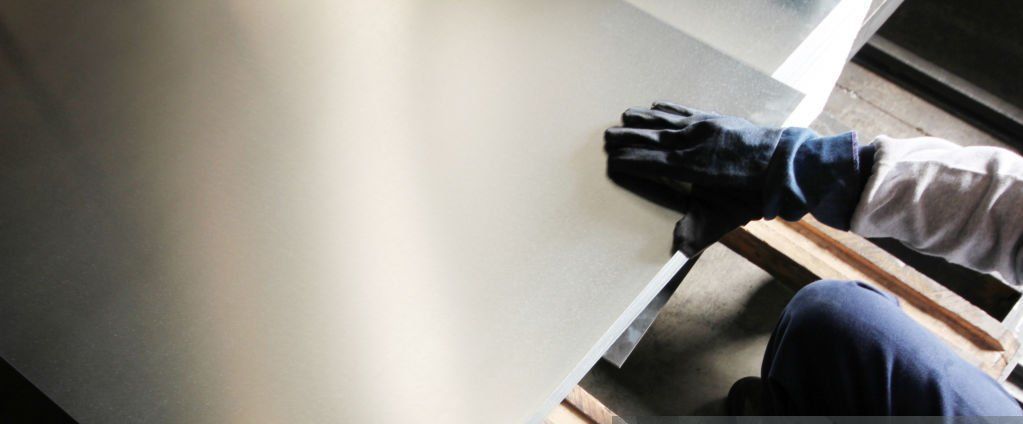 Person in gloves touching a large, shiny metal sheet in a workshop.