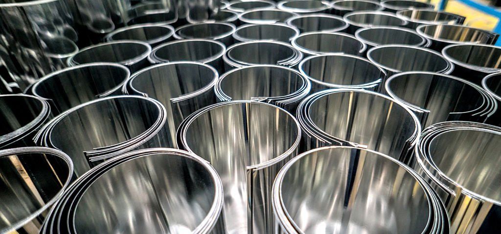 Close-up of numerous, shiny, rolled metal sheets in a manufacturing setting.