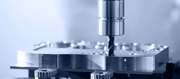 A metal-cutting machine drilling into a metal workpiece. Blue-toned with a close-up focus.