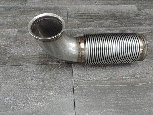 A stainless steel exhaust pipe is sitting on a tiled floor.