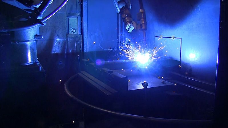 A robot is welding a piece of metal in a dark room.