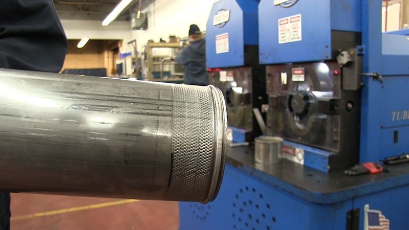 A person is holding a metal pipe in a factory.
