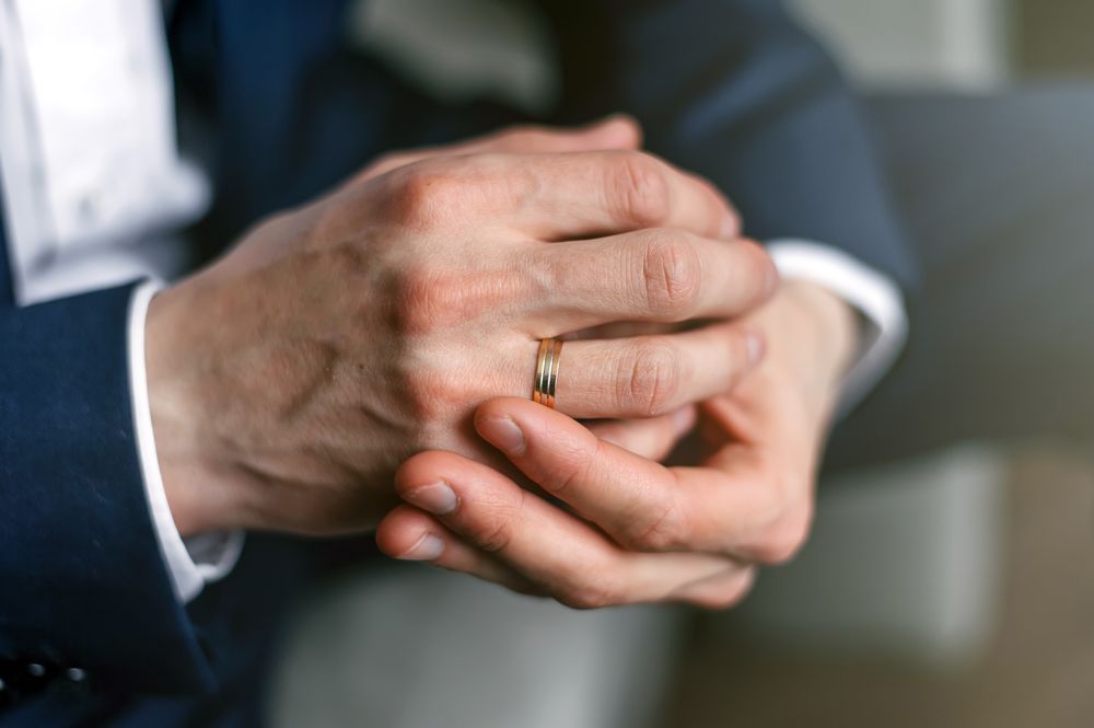 A man in a suit is putting a wedding ring on his finger.