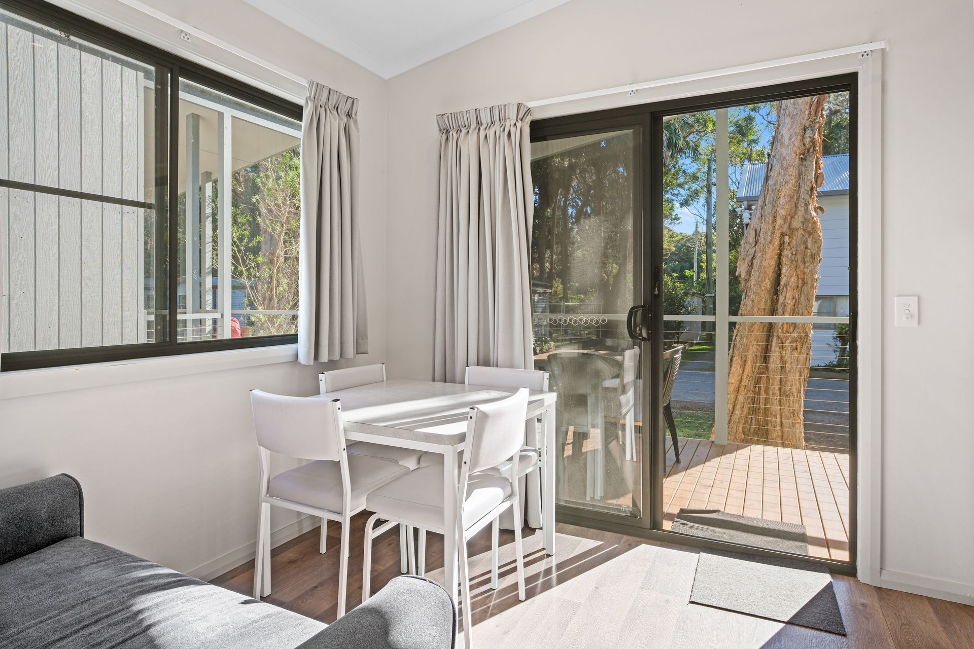 Small dining area with table and chairs near a sliding door leading to a deck.— Pacific Palms Caravan Park in Elizabeth Beach, NSW