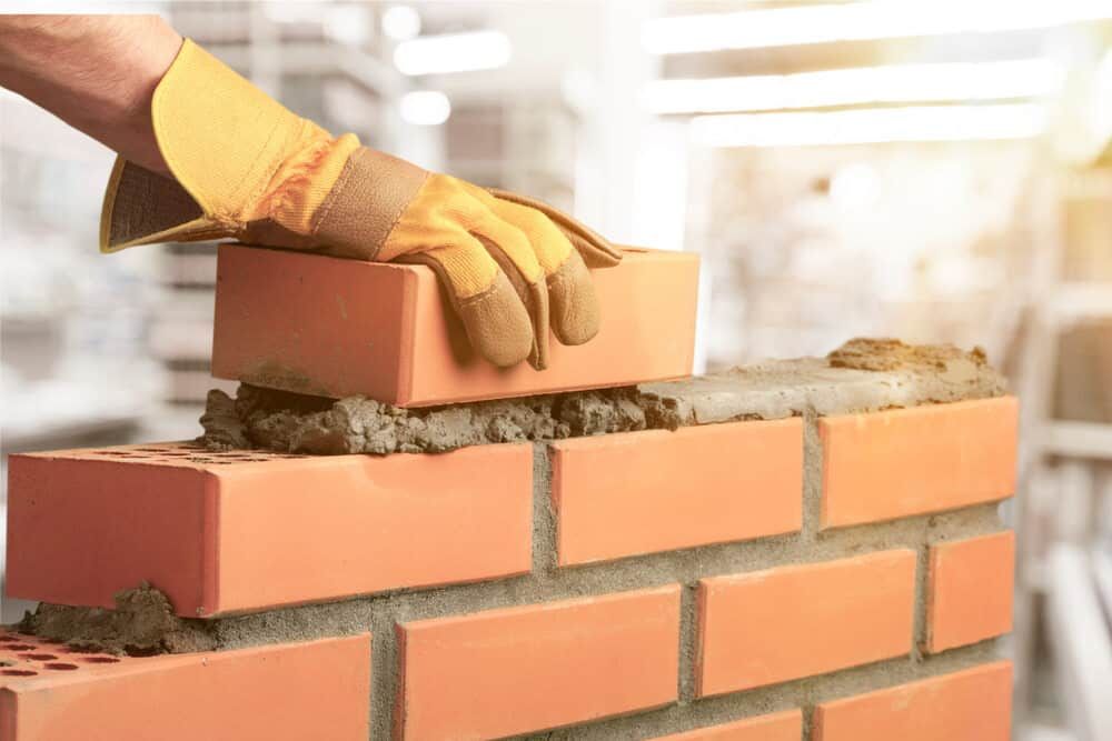 A Person Is Laying Bricks On Top Of A Brick Wall — Mascrete Pty Ltd In Hermit Park, QLD