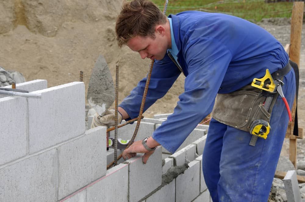 A Man In Blue Overalls Is Working On A Brick Wall — Mascrete Pty Ltd In Hermit Park, QLD