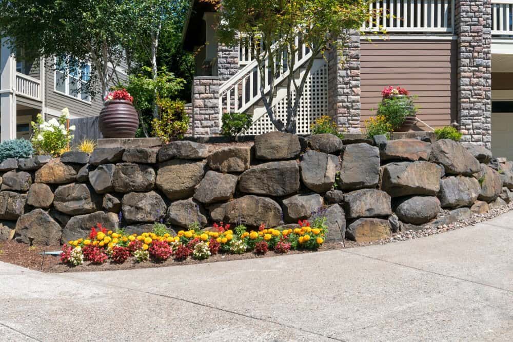 A Stone Wall With Flowers In Front Of A House — Mascrete Pty Ltd In Hermit Park, QLD