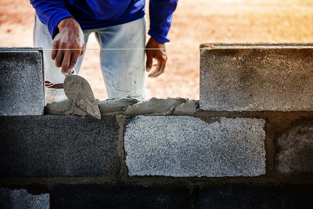 A Man Is Laying Bricks On A Wall With A Trowel — Mascrete Pty Ltd In Hermit Park, QLD