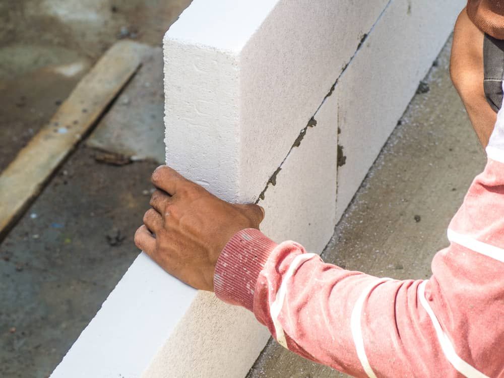 A Man Is Holding A White Brick In His Hands — Mascrete Pty Ltd In Hermit Park, QLD