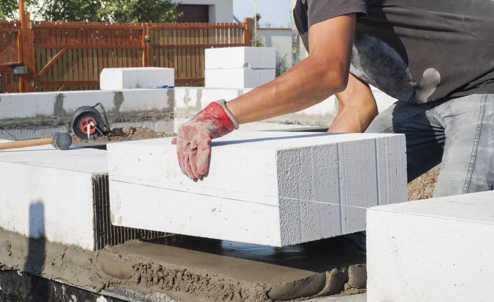 A Man Is Laying Concrete Blocks On A Construction Site — Mascrete Pty Ltd In Hermit Park, QLD