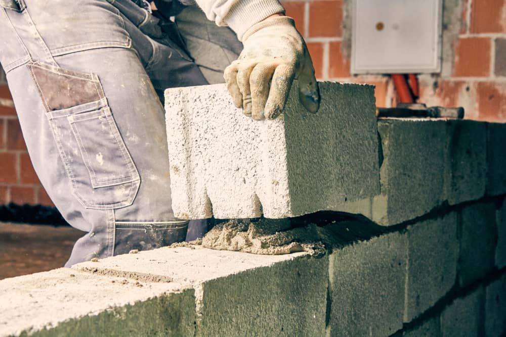 A Man Is Laying Bricks On Top Of A Brick Wall — Mascrete Pty Ltd In Hermit Park, QLD