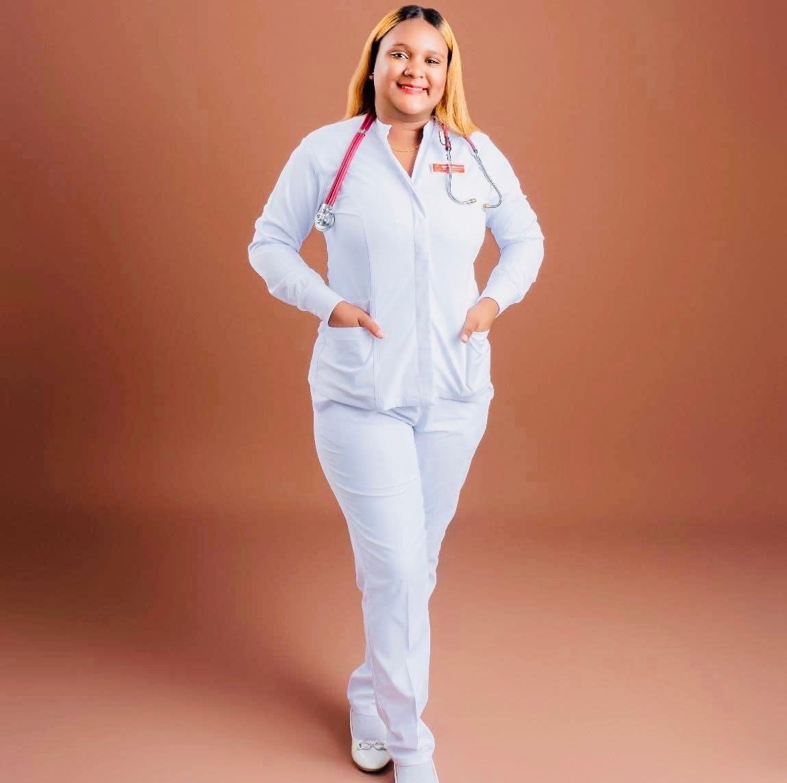 Person in a white medical uniform with red stethoscope, standing and smiling against a peach background.