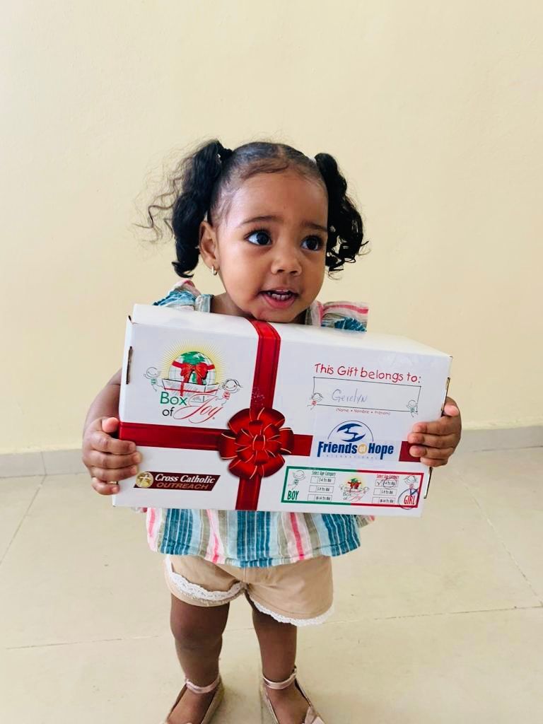 A little girl is holding a gift box with a red ribbon.
