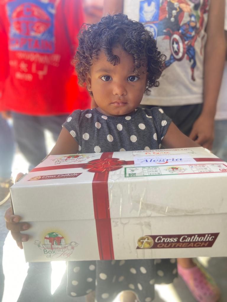 A little girl is holding a box with a red ribbon on it.