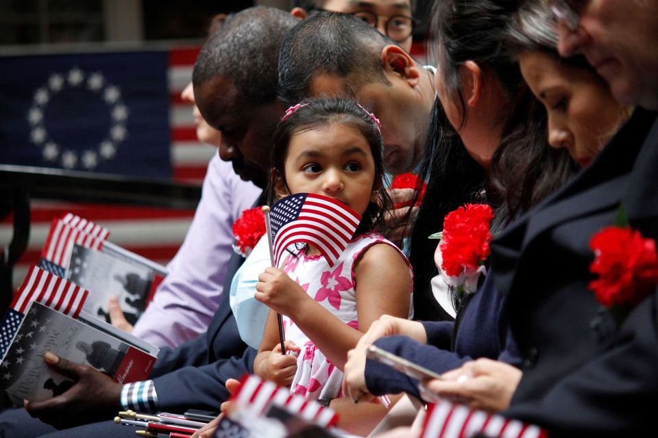 People seated in a memorial ceremony holding small American flags and red, white, and blue items