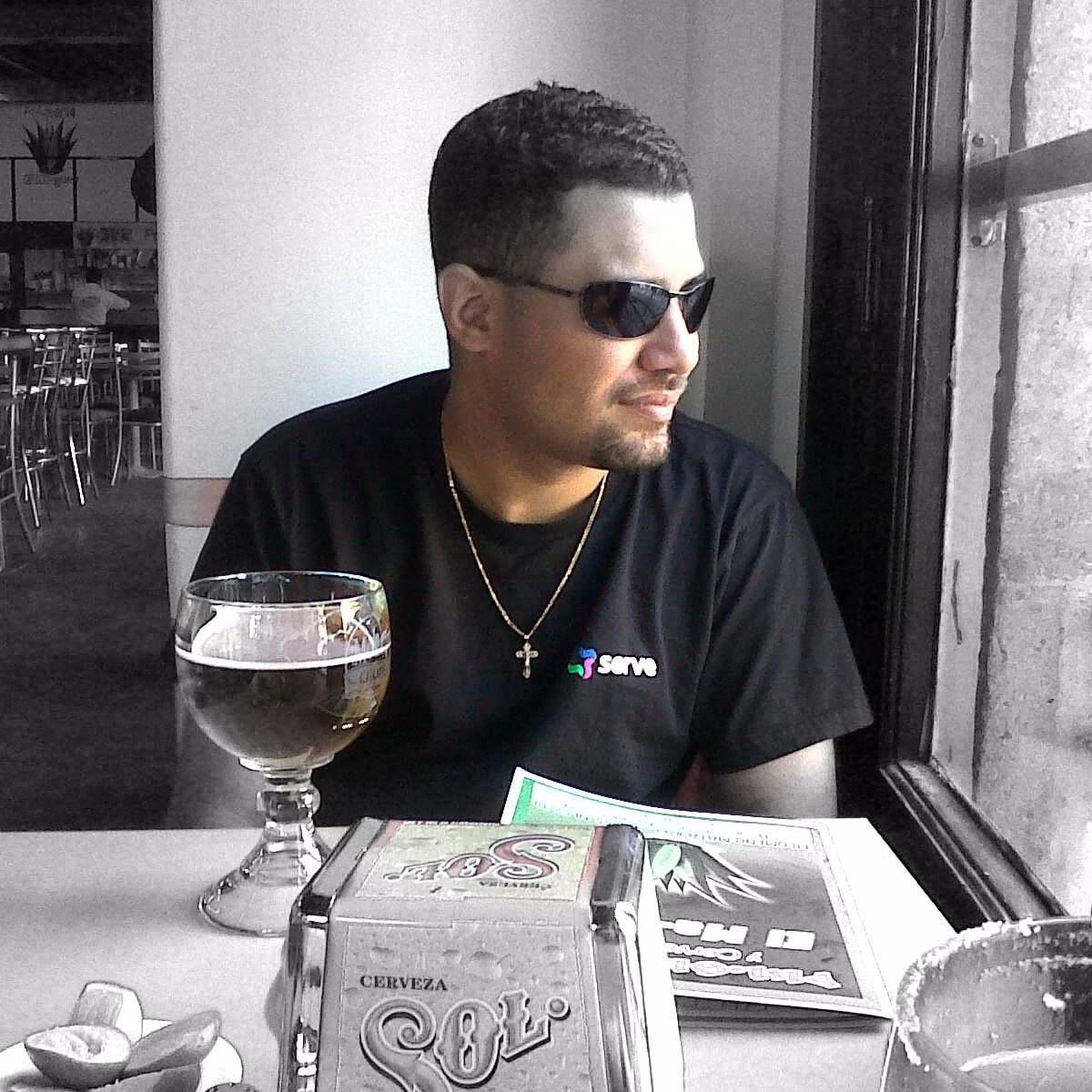 A man wearing sunglasses sits at a table with a glass of beer