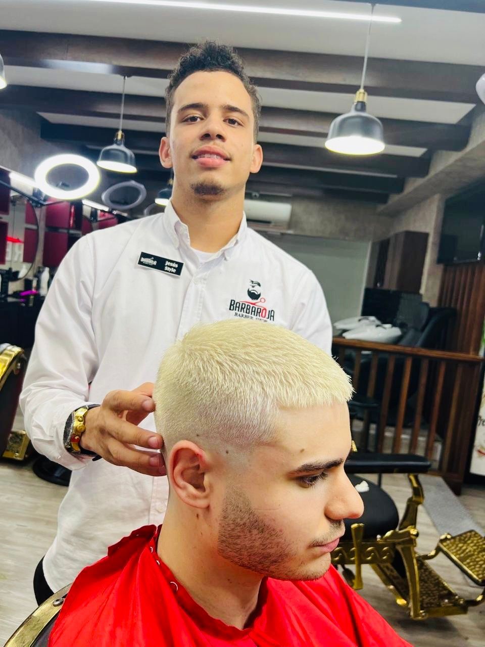Barber standing behind a client with bleached hair in a barbershop, mid-haircut