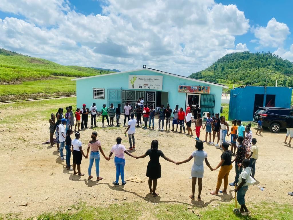 A group of people are standing in a circle holding hands in front of a building.
