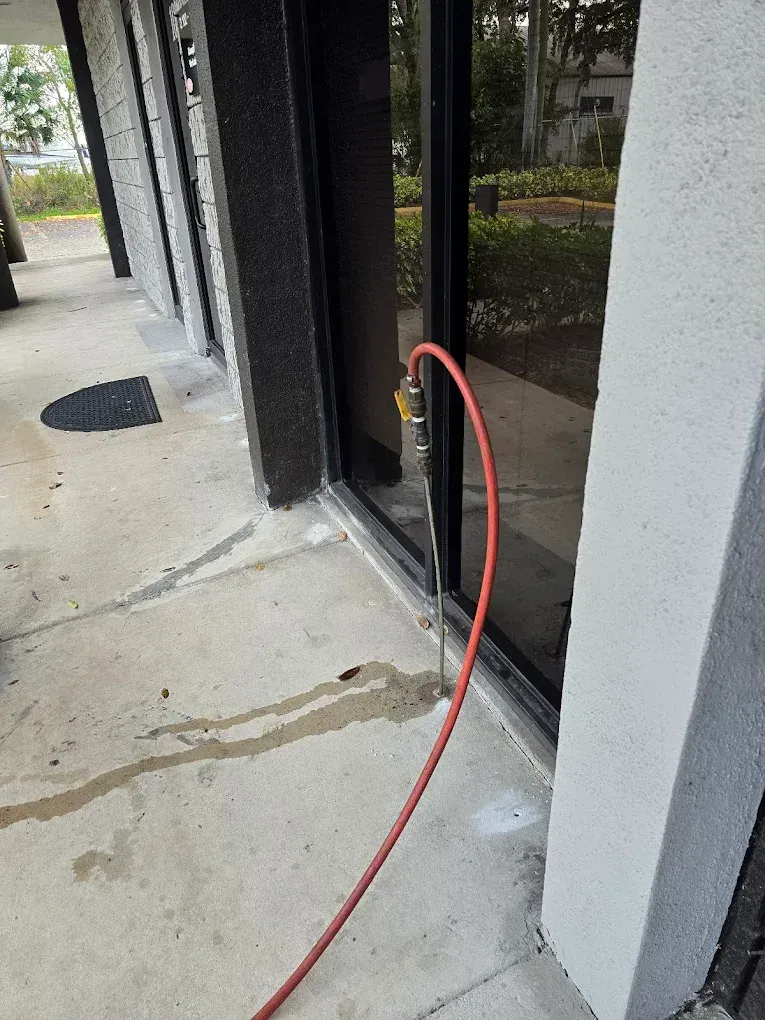 A red hose connected to a building entrance spills water onto the concrete walkway.