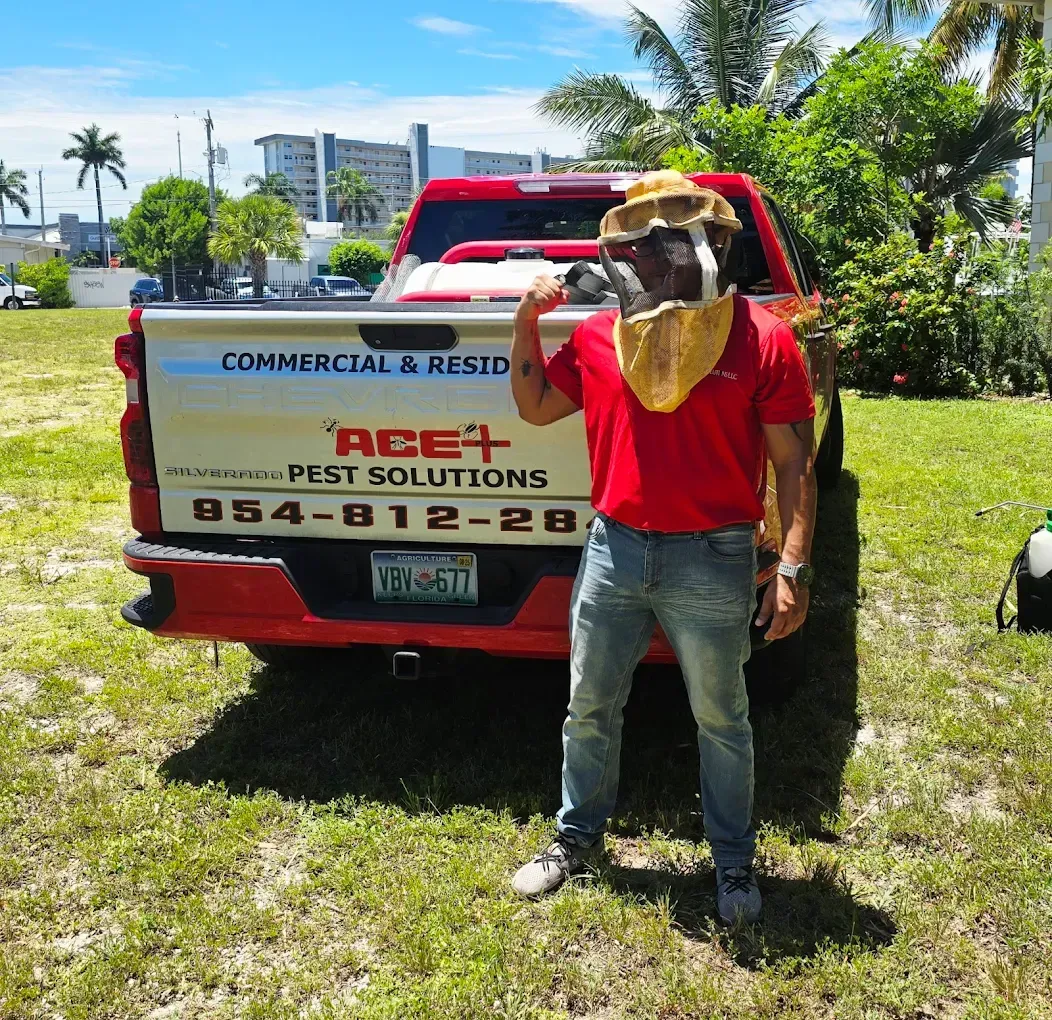 A worker in a protective bee suit stands in front of a red truck labeled 