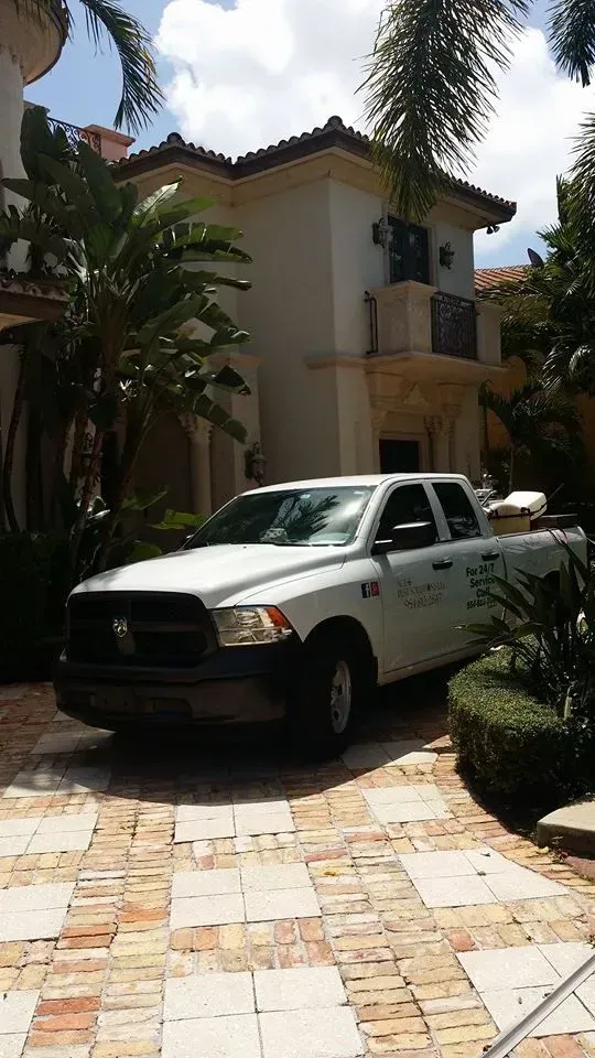 A white service truck parked in the driveway of a multi-story stucco home with palm trees in a sunny residential area.