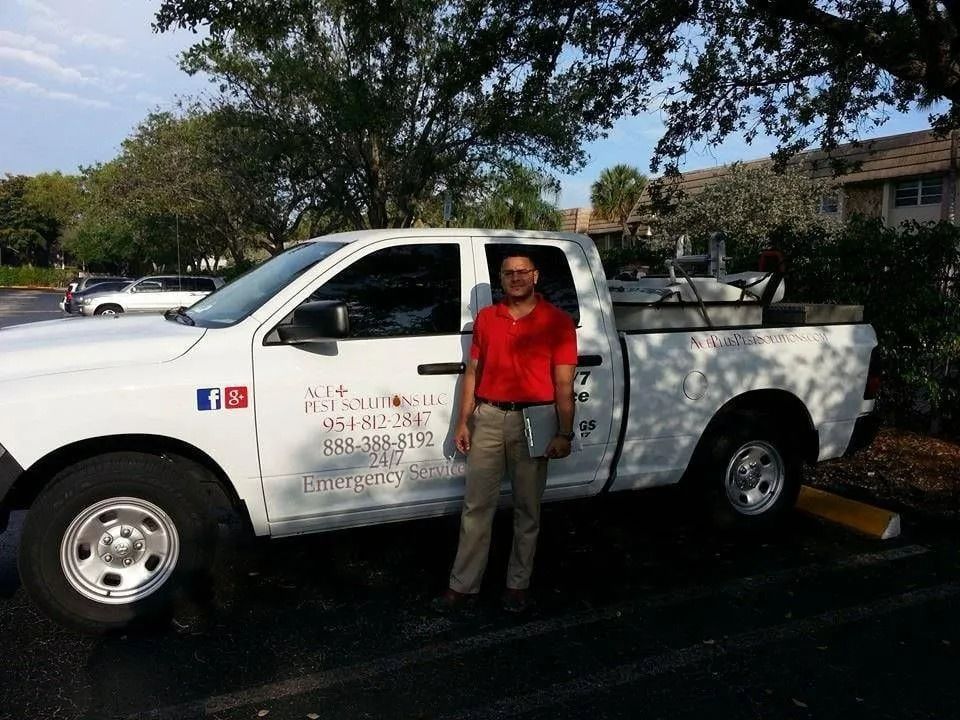 A person in a red shirt stands beside a white service truck parked in a lot under trees.