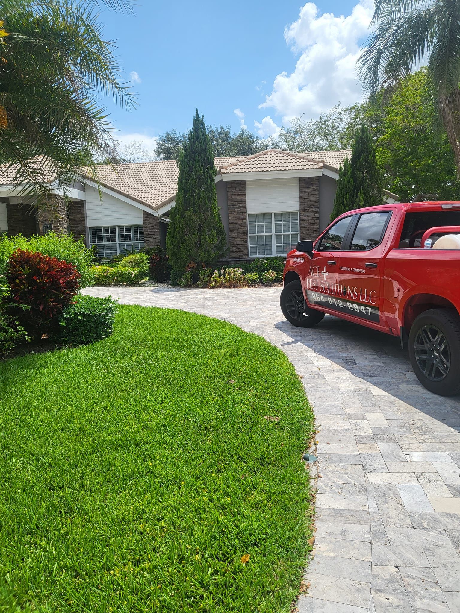A bright red pickup truck parked on a paved driveway in front of a suburban house surrounded by green landscaping.