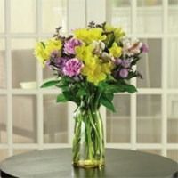 Mixed bouquet of yellow, pink, and purple flowers in a clear glass vase on a table