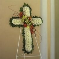White floral cross arrangement with red accents on a stand indoors