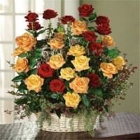 Basket of red and yellow roses with greenery in a white woven vase