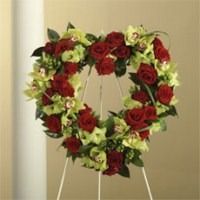 Heart-shaped red rose and green floral wreath on a stand against a beige wall