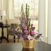 Pink and purple floral arrangement in a gold vase on a table near a window