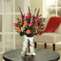 Pink and red flower arrangement in a vase on a round table with a white ribbon, in a living room