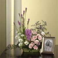 Flower arrangement beside a framed black-and-white photo on a table against a beige wall.
