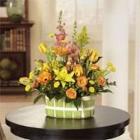 Colorful flower arrangement in a green vase on a round black table in a softly lit room