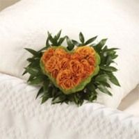 Heart-shaped orange rose bouquet on a white quilted pillow with green leaves